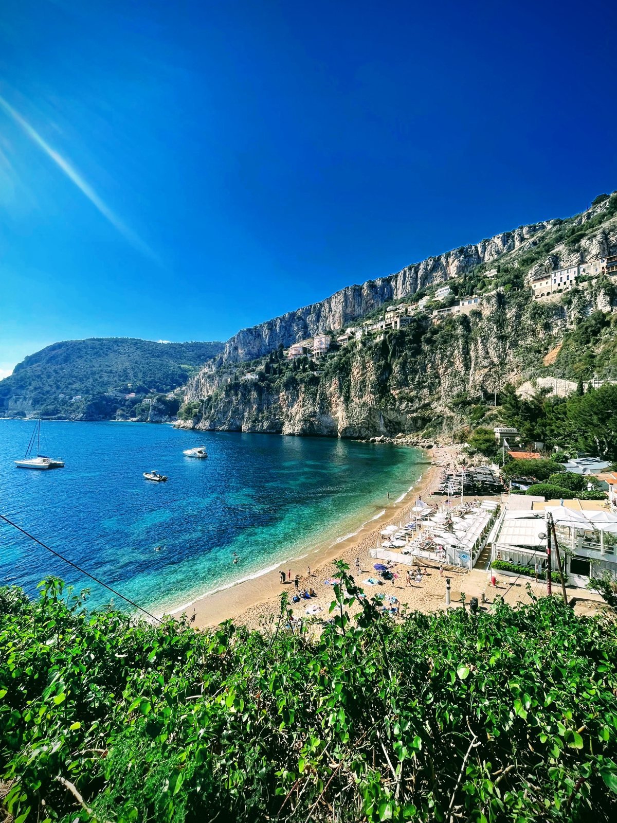 La crique de la Plage Mala à Cap-d'Ail vue d'en haut, avec les falaises, les plages privées et des bateaux sur l'eau turquoise