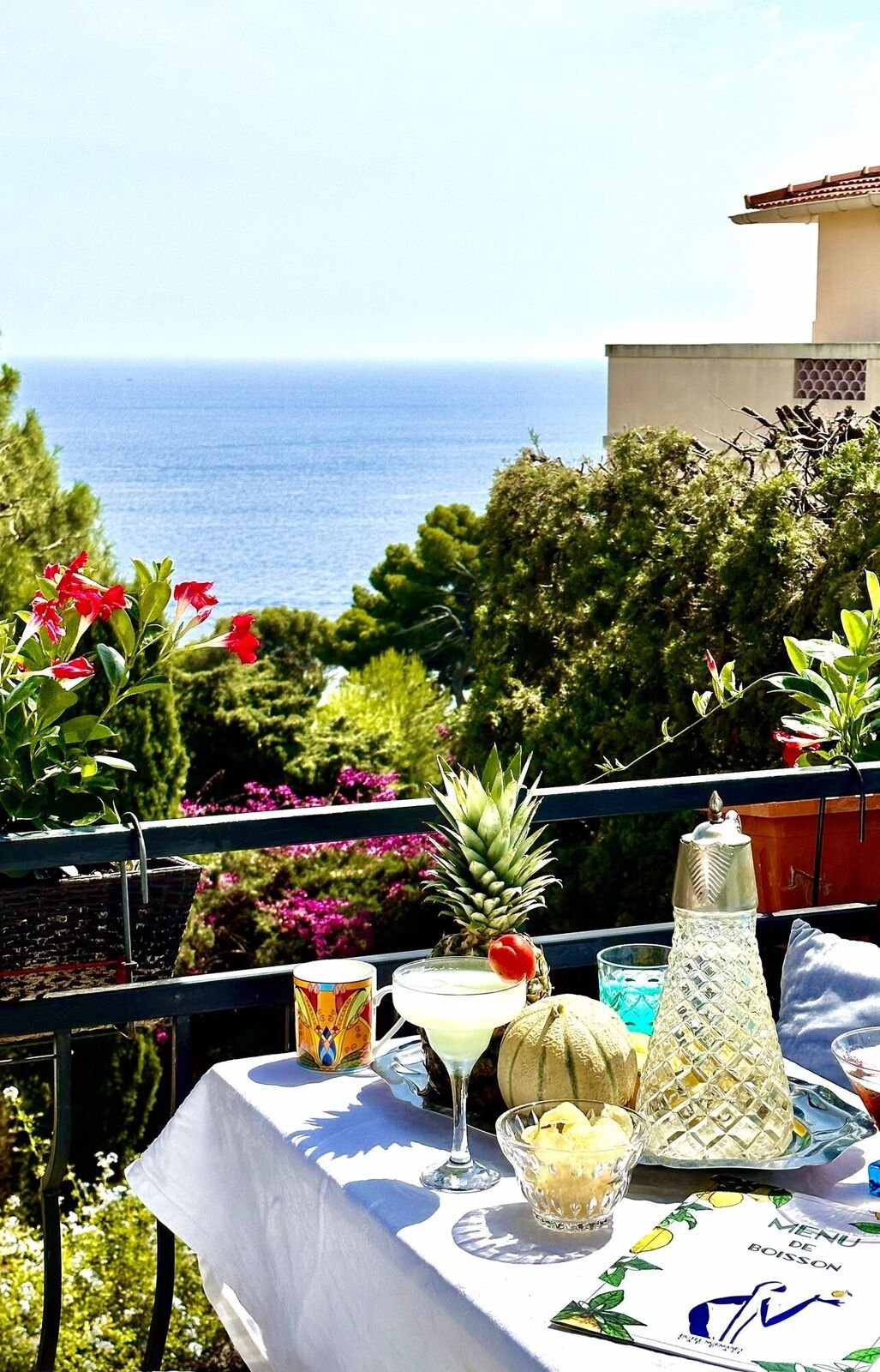 A glass of café crème held up against the sea on the terrace